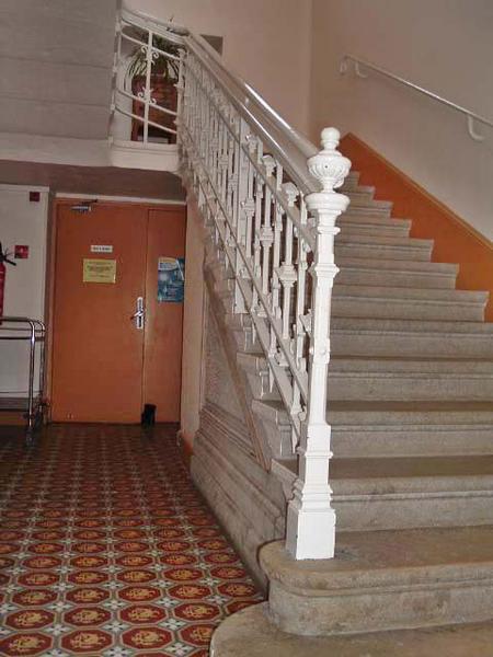 Vue intérieure, escalier en fonte au départ du rez-de-chaussée et carrelage en ciment.