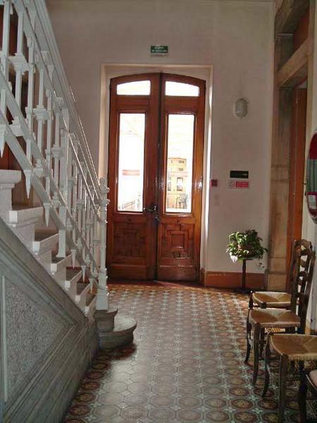 Vue générale intérieure du rez-de-chaussée, aile droite, avec escalier, carrelage et porte d'entrée.