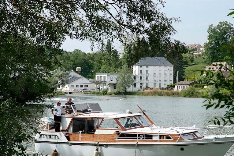 Les bâtiments modernes du moulin vus d'amont. Bateau de plaisance au premier plan.