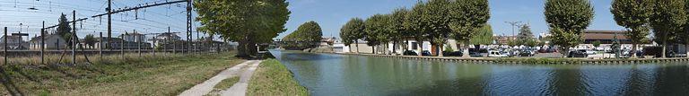 Panorama du canal traversant Migennes en direction de l'Yonne. A gauche, le site SNCF et la gare, à droite, la ville reconnaissable à ses halles.