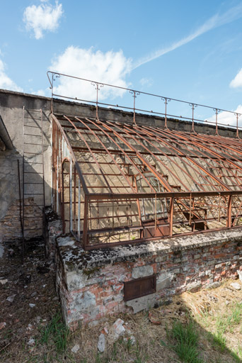 Détail de la structure métallique construite sur un muret en brique et adossée à un mur en calcaire.