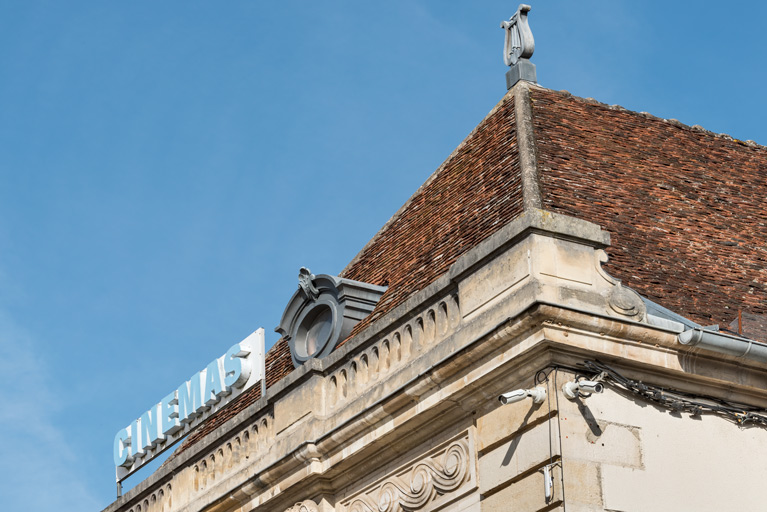 Façade antérieure : partie supérieure, vue de trois quarts, avec enseigne et épi de faîtage en forme de lyre.