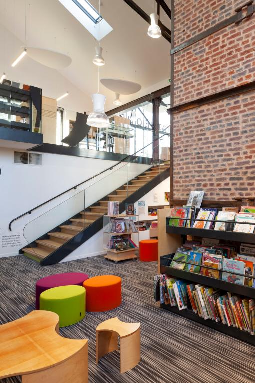 Bâtiment après reconversion : Médiathèque, espace inférieur dédié à la litterature jeunesse avec massif de la cheminée.
