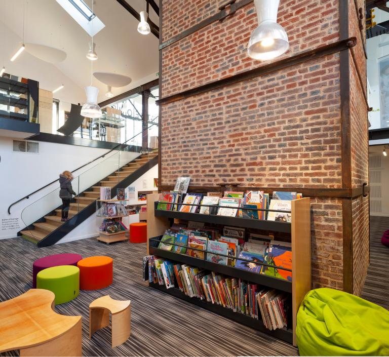 Bâtiment après reconversion : Médiathèque, espace inférieur dédié à la litterature jeunesse avec massif de la cheminée.