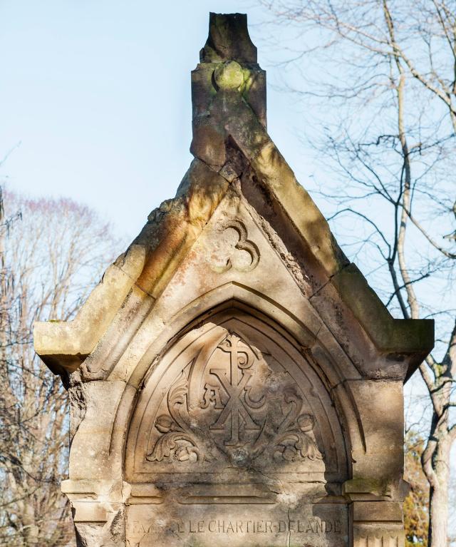 Détail du fronton du tombeau en forme de chapelle de la famille Lechartier-Delande sculpté de symboles religieux et funéraires : fleurs de pavot, chrisme, alpha et oméga.