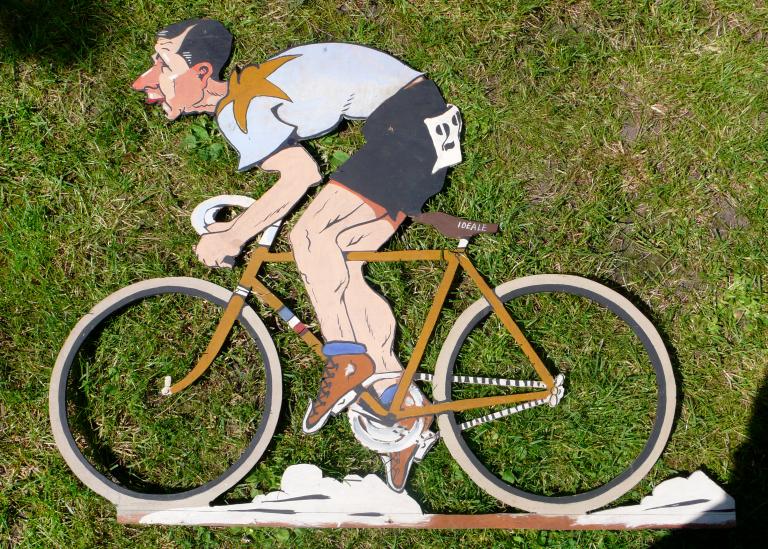 Enseigne publicitaire pour la selle Idéal, caricature de Marcel Berthet à vélo (Coll. part.).