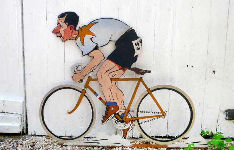 Enseigne publicitaire pour la selle Idéal, caricature de Marcel Berthet à vélo (Coll. part.).