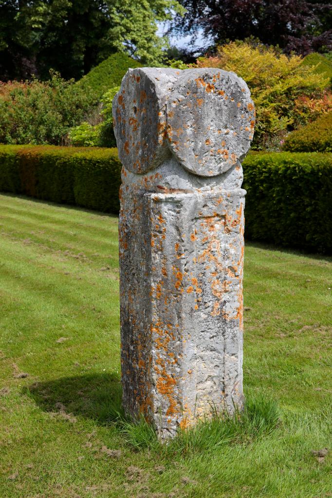 Pilier de pierre monolithe placé au milieu des parterres. 