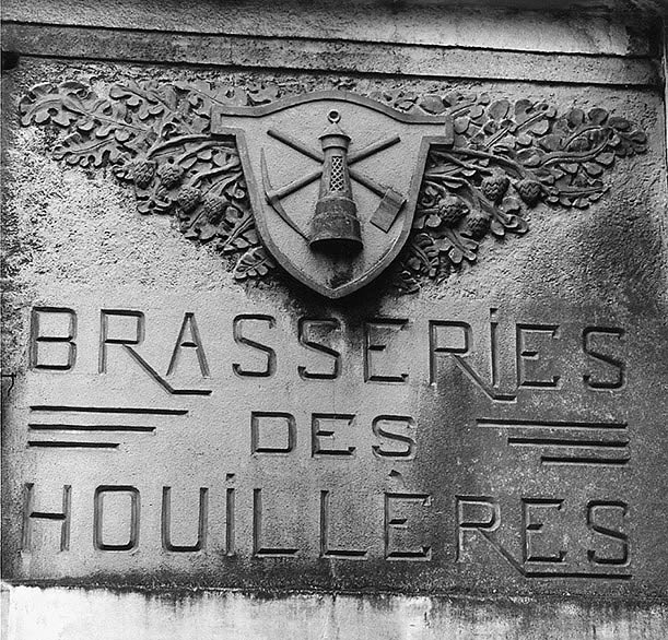Entrée de la brasserie : insigne du mineur sur fond de feuilles et cônes de houblon.