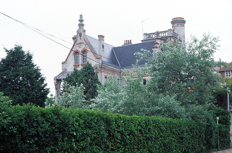 Vue de trois-quarts de la villa derrière sa haie depuis la rue Jean Monnet.