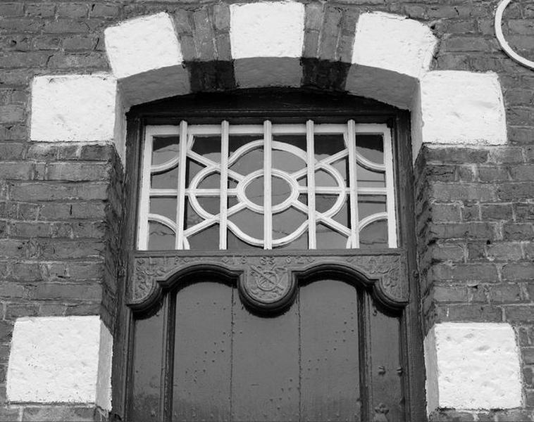 Détail de la porte : l'imposte vitrée et le linteau chantourné sculpté.