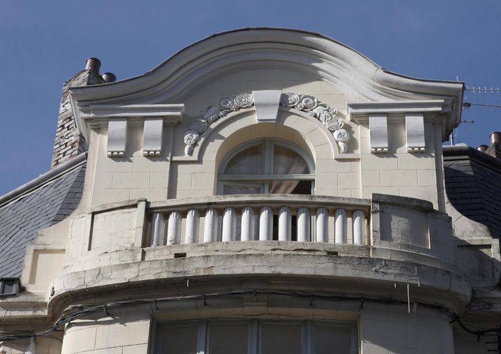 Détail du fronton orné d'une couronne de fleurs en aplat et d'agrafes aux extrémités géométriques.