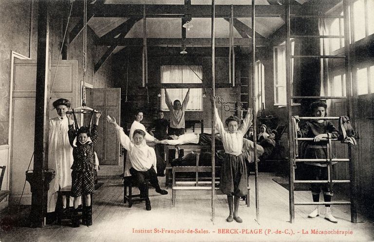 Bâtisse provisoire en bois abritant la salle de gymnastique et de mécanothérapie, vue intérieure montrant des filles occupées à des exercices de gymnastique orthopédique. Carte postale, début du 20e siècle (coll. part.).