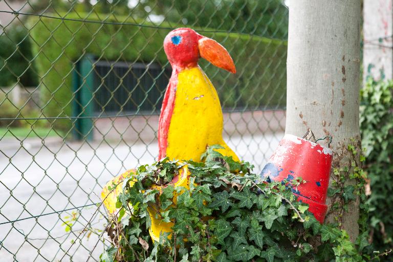 Figure en ciment représentant un perroquet installée devant la maison.