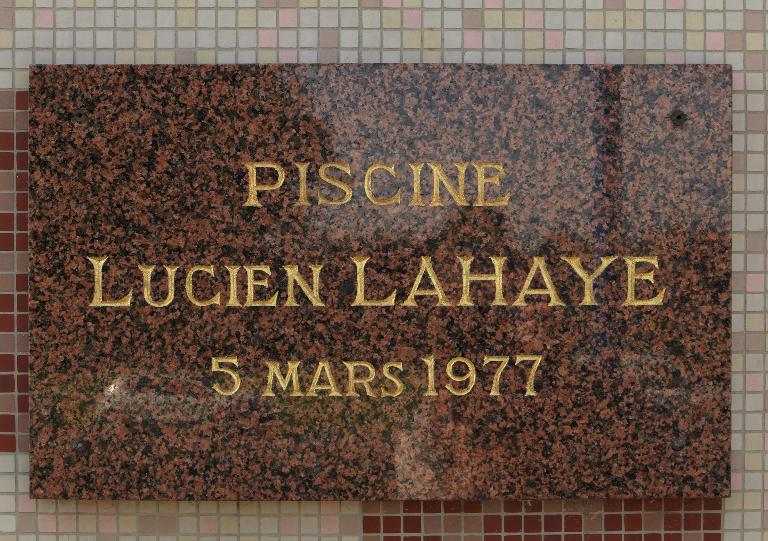 Plaque à l'entrée de la piscine portant le nom et la date d'inauguration. 