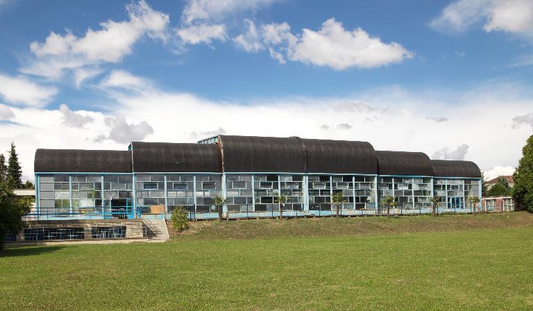 Vue générale de la façade sud, donnant sur une terrasse et une pelouse (servant de solarium et d'aire de jeux aux beaux jours). ; Noyon (Oise). La piscine Paul-Boutefeu construite sur les plans des architectes Claude Charpentier et Jean Tabanou et inaugurée en 1968.