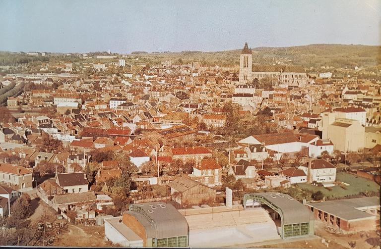 Vue aérienne de la ville de Noyon, avec au premier plan la piscine. Dernière de couverture de la brochure de présentation de la piscine de Noyon réalisée par la société MacGregor-Comarain. Photo : H. Bernard (AN ; 19940528/1).