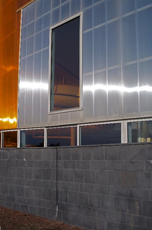 Détail d'une ouverture et des panneaux de revêtement plastique en façade; soubassement en grès cérame noir. 