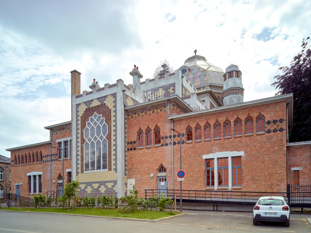 Vue d'ensemble oriental de l'église, avec le chevet au centre, flanqué de la sacristie et de la salle des catéchèses en brique orangée.