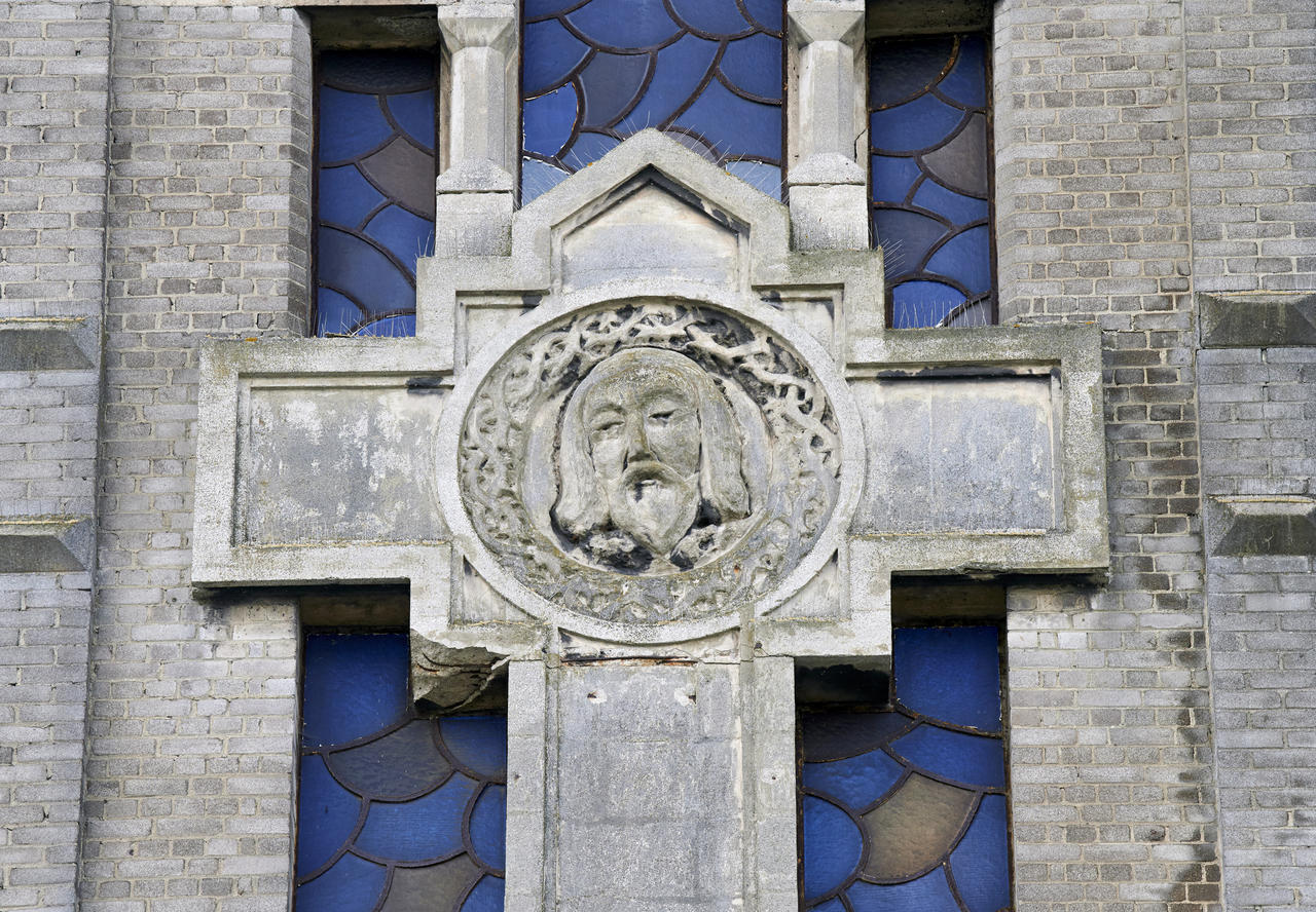 Détail de la croix en béton qui orne l' élévation nord du clocher : le visage du Christ.