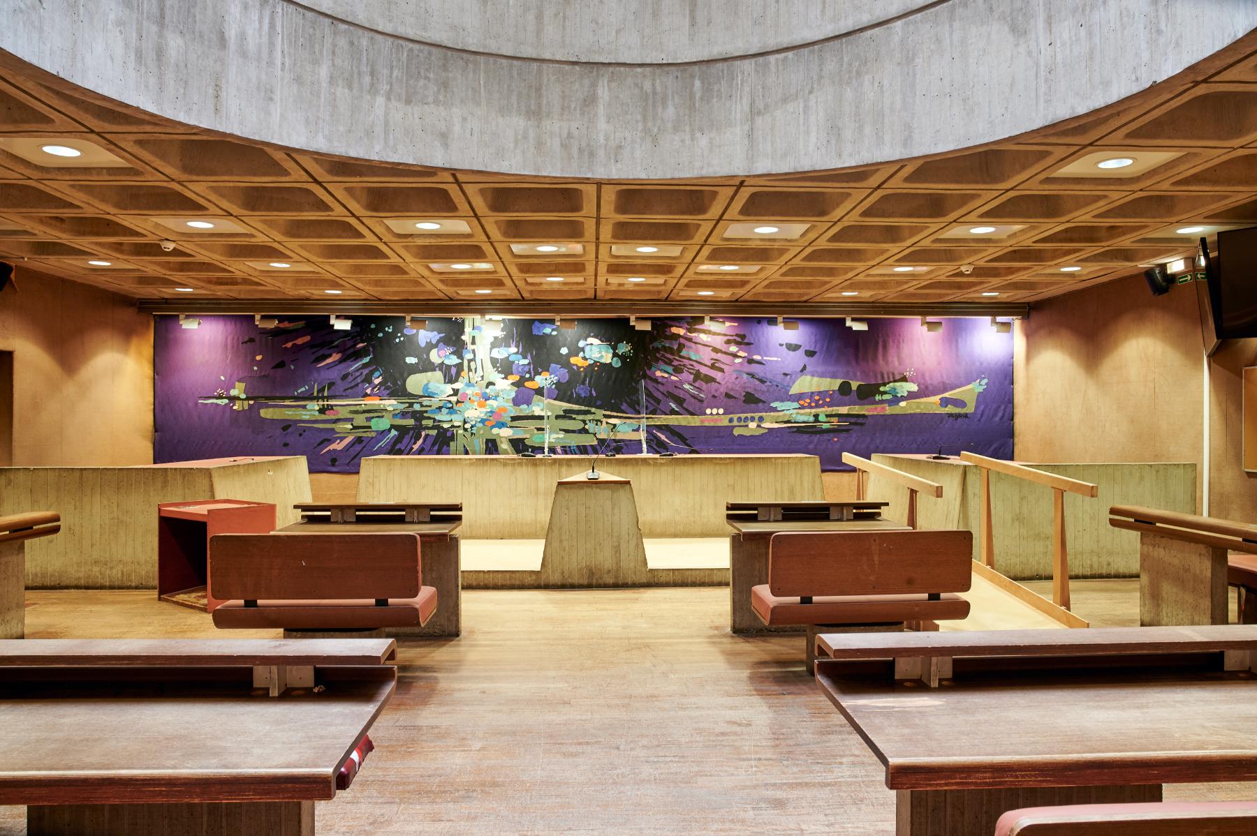 Ancienne petite salle d’audience du tribunal d’instance du rez-de-chaussée bas, vue de face. Derrière l’estrade des juges, la tapisserie de Michel Degand, « D’étoiles dans les soirs tremblants ».