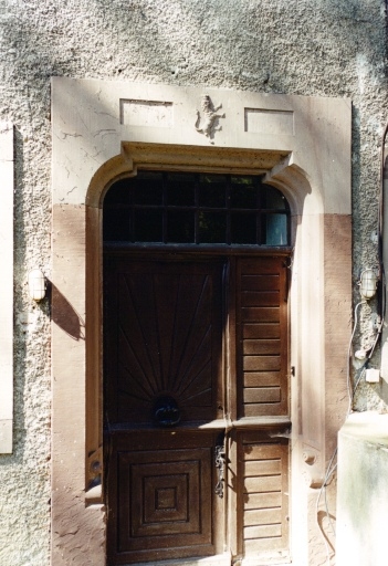 Porte avec emblème héraldique sculpté dans la masse, façade est de la demeure.