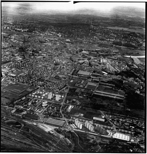 Vue aérienne : la ville vue du nord. La gare du Nord au premier plan, l'usine D.M.C. à droite et la Cité à gauche.