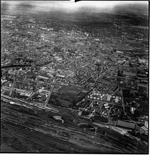 Vue aérienne : la ville vue du nord. Au premier plan : la gare du nord, la filature peignée Gluck au centre, derrière elle la Cité.