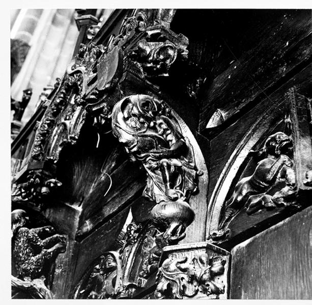 Mur sud du choeur, stalles hautes, 2ème groupe, console 5 : homme assis se cachant derrière une feuille.