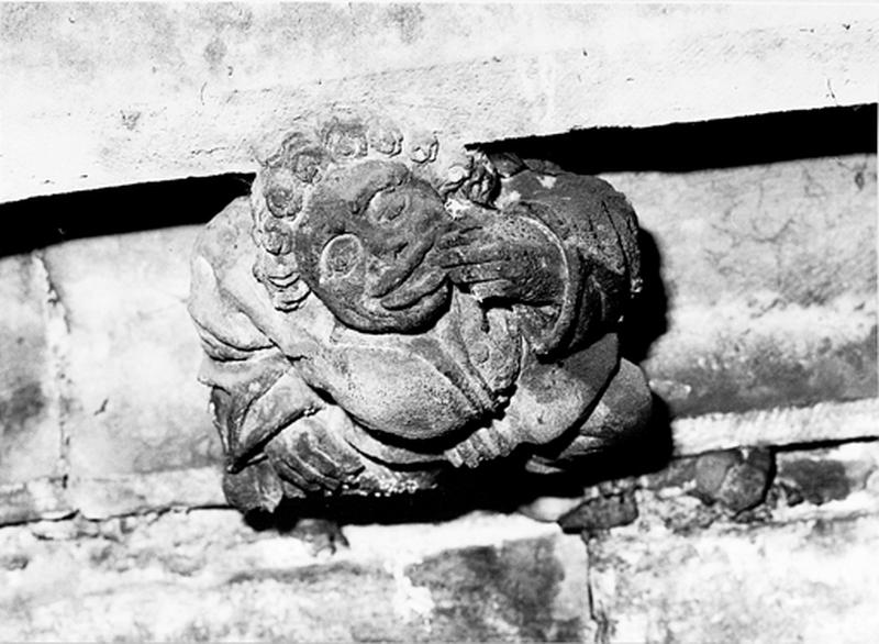 Façade sud, relief sur la corniche du bas côté, caché par la chapelle de la Vierge : homme grimaçant portant une main à la bouche (S5)