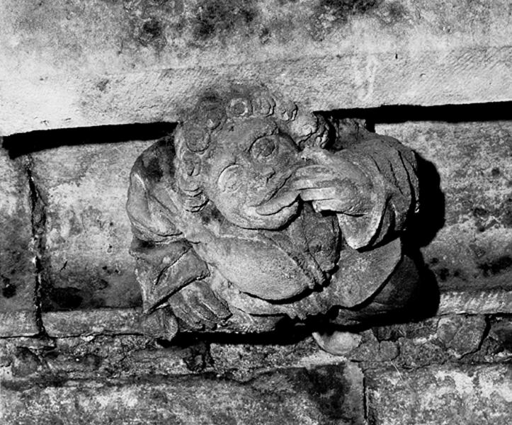 Façade sud, relief sur la corniche du bas côté, caché par la chapelle de la Vierge : homme grimaçant portant une main à la bouche (S5)