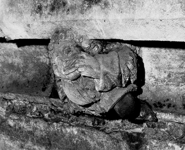 Façade sud, relief sur la corniche du bas côté, caché par la chapelle de la Vierge : homme grimaçant portant une main à la bouche (S5)