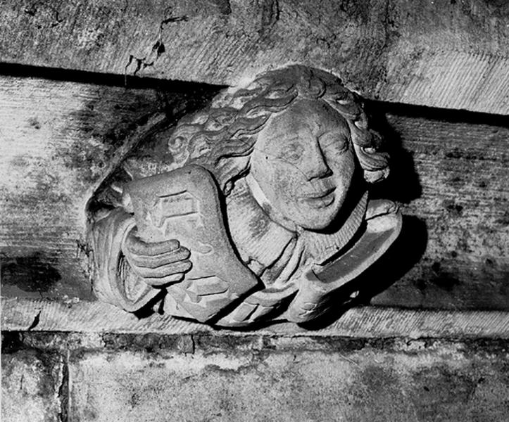 Façade sud, relief sur la corniche du bas côté, caché par la chapelle de la Vierge : jeune homme tenant un phylactère (S4).