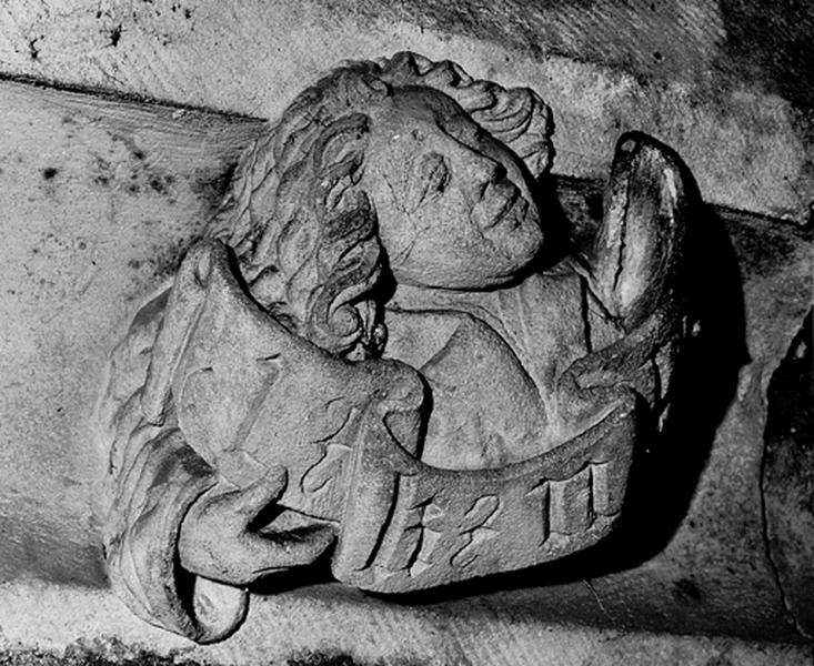 Façade sud, relief sur la corniche du bas côté, caché par la chapelle de la Vierge : jeune homme tenant un phylactère (S3).