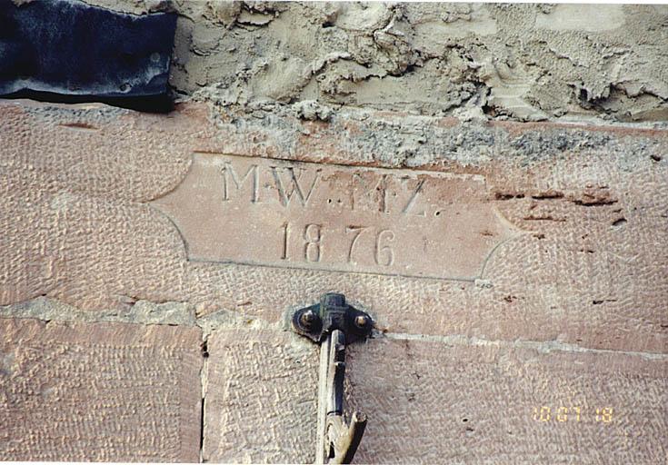Hangar. Détail de la chaîne d'angle formant montant pour la porte charretière avec date 1876.