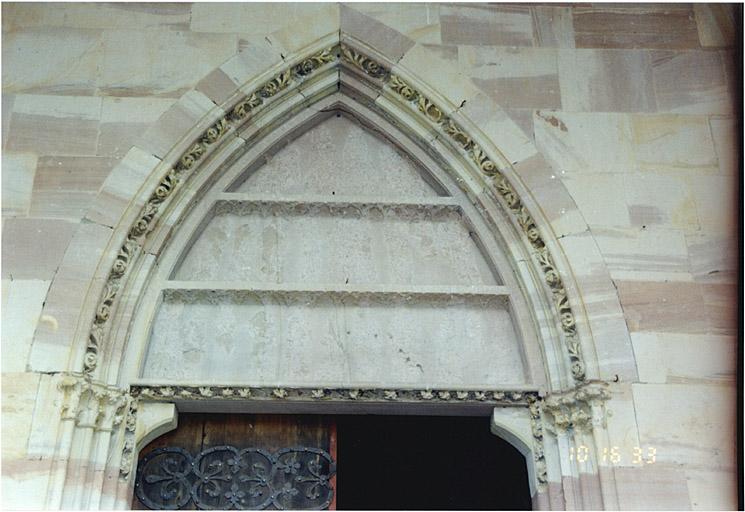 Porte du porche, vers le collatéral sud. Vue du tympan avec traces des sculptures ayant représenté l'origine divine de la fondation de l'abbaye par le roi Dagobert.