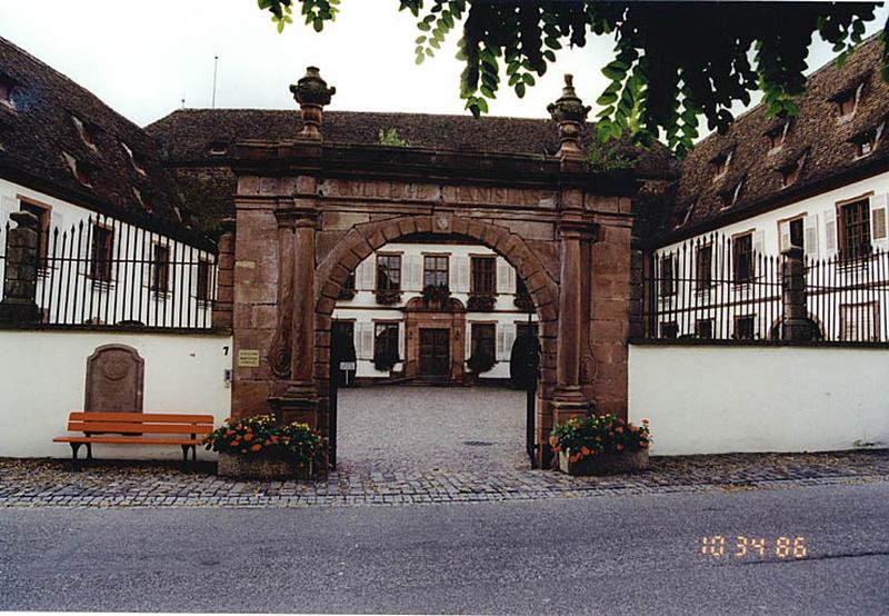 Vue d'ensemble depuis la rue de la porte fermant la cour, du corps de bâtiment principal, sud, et des 2 ailes en retour, côté est et ouest.