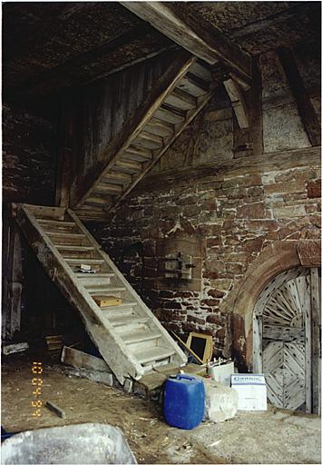 Vue du mur de la cave, sous le hangar, avec escalier vers l'étage.