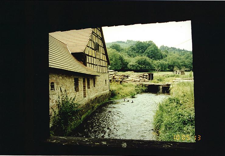 Vue depuis la passerelle sur la Sauer, de l'élévation postérieure sur la rivière, de la dépendance en rez-de-chaussée et de la grange.