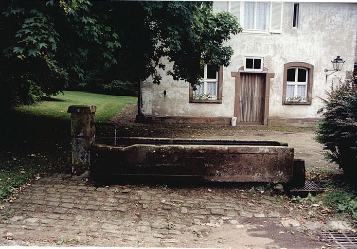 Fontaine devant l'ancienne maison de bûcheron et de cocher avec remises.