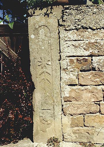 Vue de la ferme, 48 rue de l'Eglise, piédroit de la porte charretière, sculpté d'une roue et d'une fleur.
