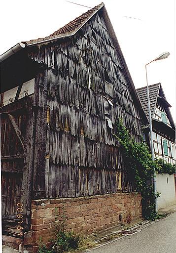Vue de la ferme, 5 rue des Frères, mur-pignon de la grange, couvert de bardeaux de bois pointus.