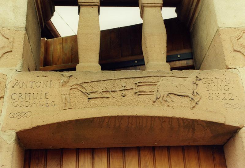 Ferme, 208 rue Principale : linteau de la porte piétonne, sculpté d'un paysan poussant sa charrue, tirée par deux chevaux.