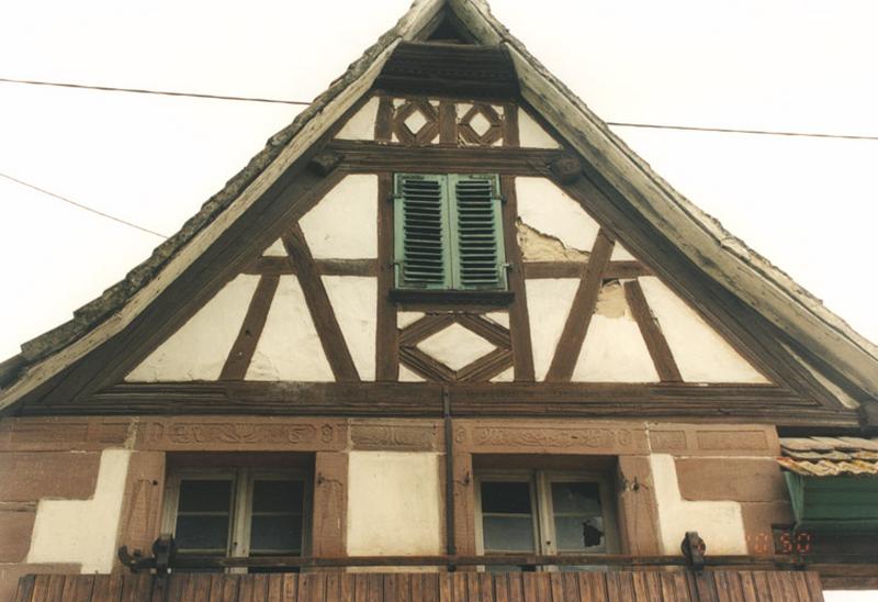 Etable, mur-pignon sur rue, fenêtres de l'étage aux chambranles sculptés.