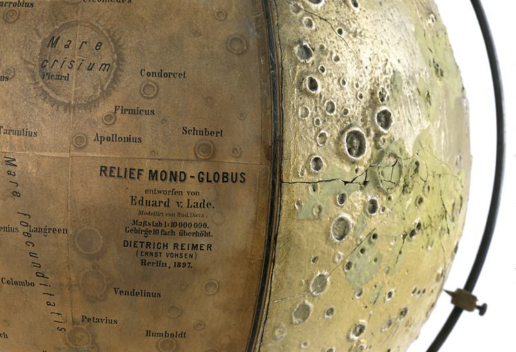 Vue de détail de l'inscription concernant les fabricants sur la face imprimée à gauche, et de la face moulée en relief avec le méridien en fer à droite.