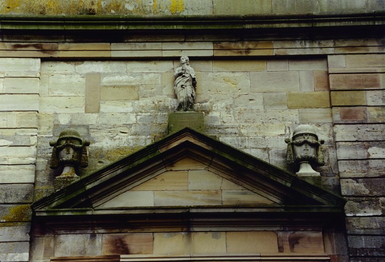 Fronton du portail. Statue de saint Jean, vers 1832 ; urnes vers 1928.