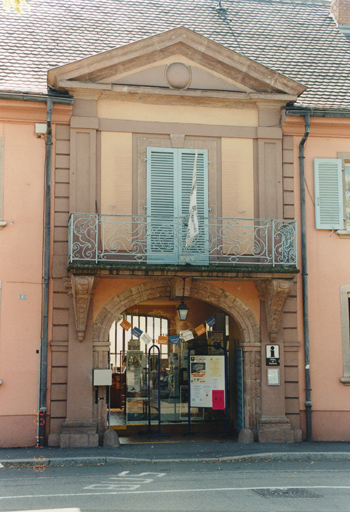 Vue partielle de la façade : avant-corps central avec fronton, porche d'entrée surmonté d'un balcon sur consoles.