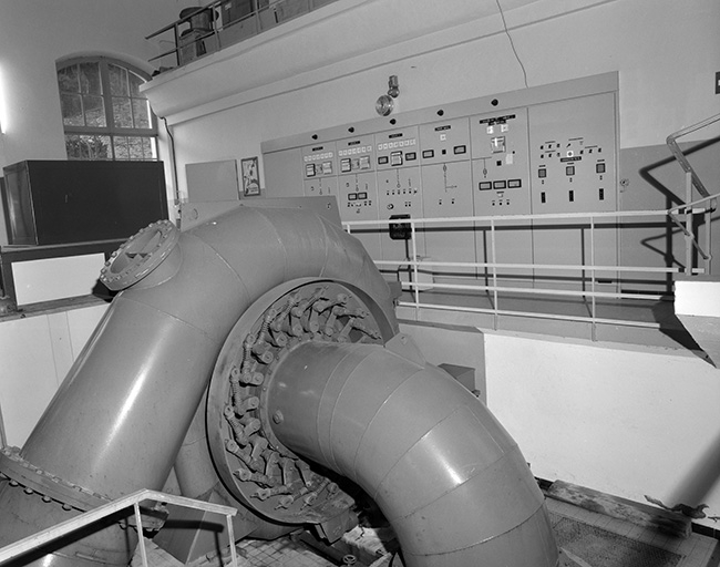 Intérieur de la centrale : turbine verticale et tableau électrique.