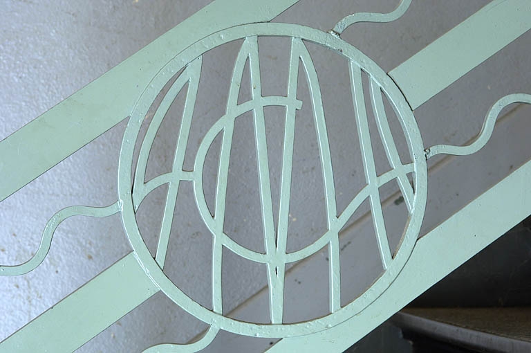 Bureau d'études. Détail du sigle ACMH sur le garde-corps de l'escalier.