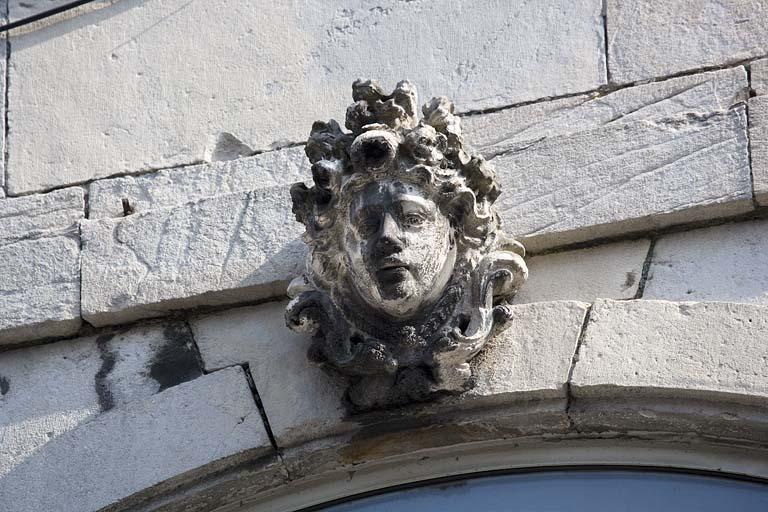 Détail de la clé d'une fenêtre au premier étage sur rue : figure coiffée d'une couronne de fleur.